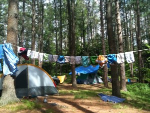 cloth diapers drying on a clothes line in the woods with a tent in the background